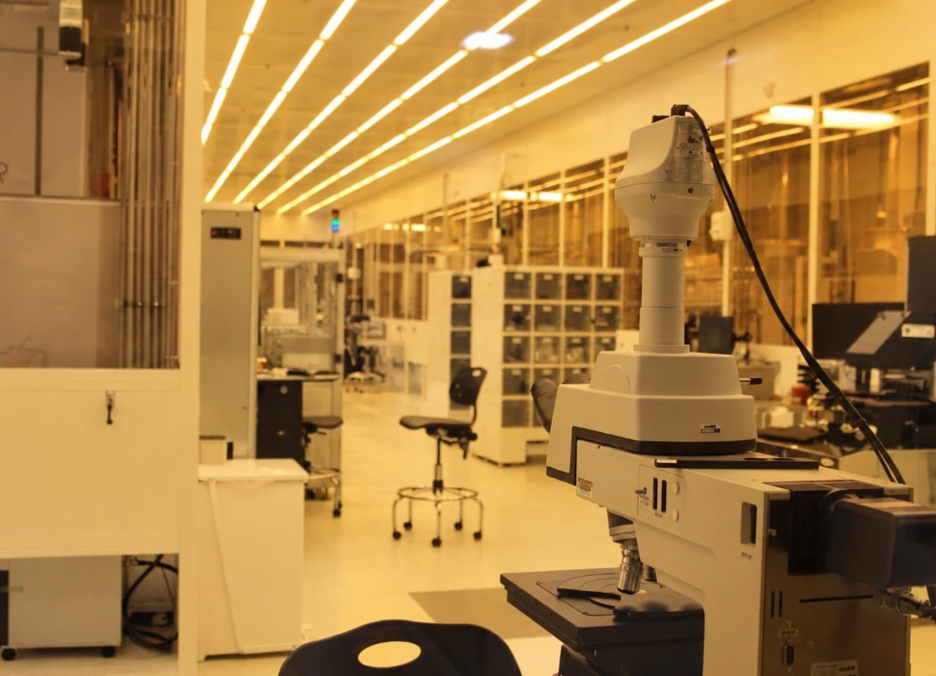 A metrology laboratory with a robotic measuring arm on a bench, instrument cabinets down one side and a lit ceiling running the length of the room