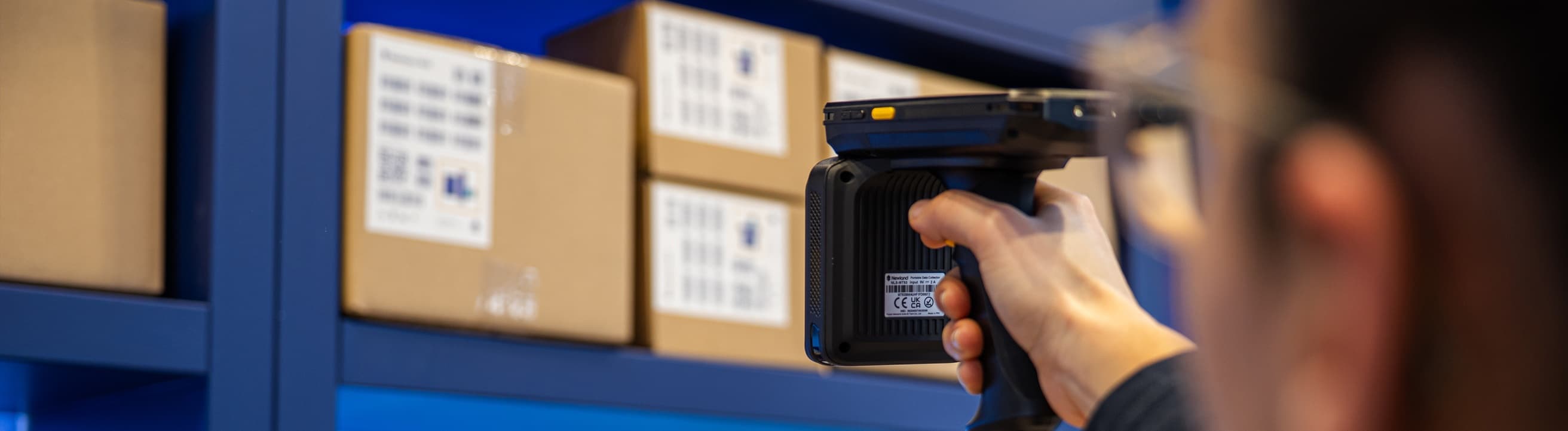 A warehouse operative scanning a shelved carton with a Newland handheld RFID reader